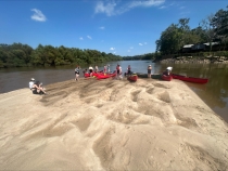 photo of people on sandbar in river with kayaks, day