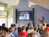 photo of man speaking, with screen, audience