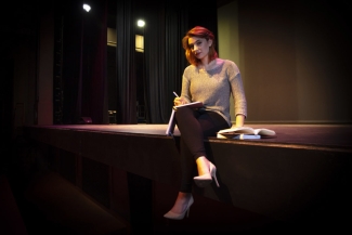 photo of woman sitting on stage with book and pen