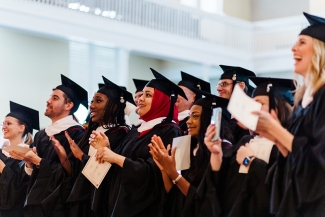 students standing and clapping in cap and gown