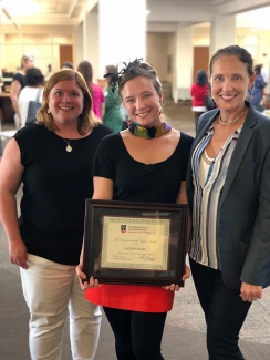 photo of three women, the middle holding a framed certificate