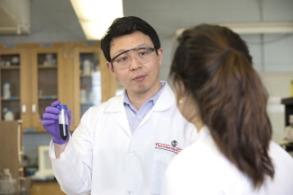 photo of two people in lab coats, foreground figure with back turned to camera