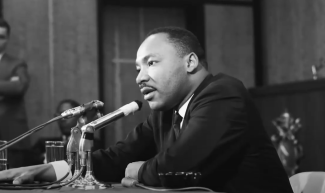 black and white photo of man seated at table with microphone