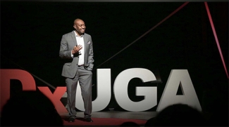 photo of man on stage talking to an audience in foreground