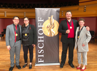 photo of four people with medals and banner in performance hall