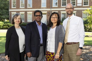 photo of four people, with Old College in background