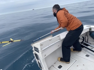 photo of man on boat in ocean with tool reaching for drone in water