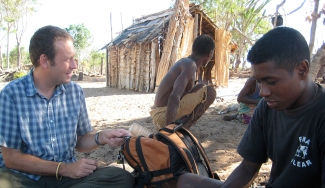 photo of three men with hut in background, day