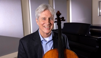 photo of man with cello, piano in background