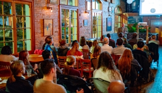 photo of man speaking to seated crowd in a coffee house