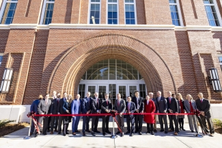 photo of group cutting ribbon in front of building, day