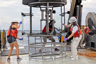 photo of equipment and people on board a ship, sea in background, day