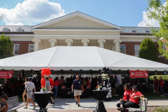 wide photo of tent event with people, building, blue sky