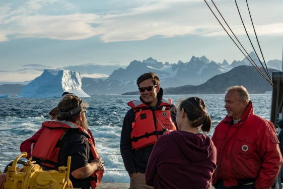 photo of people on ship, mountains in background, day