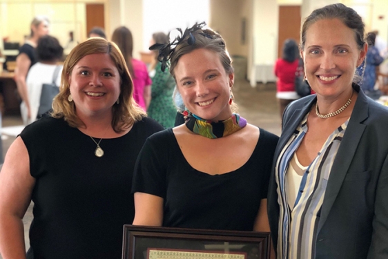 photo of three women, the middle holding a framed certificate