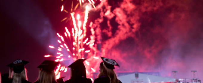 photo of people in caps and gowns, with fireworks in background