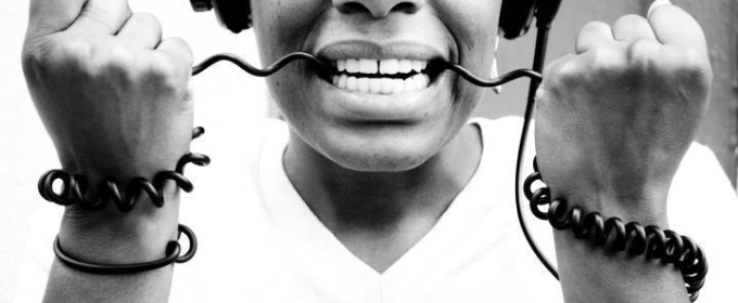 black and white photo of woman wearing headphones with the cord in her teeth