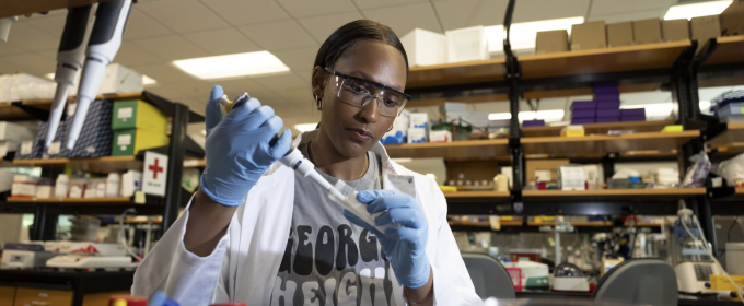 photo of woman working in lab with pipette, gloves, safety glasses