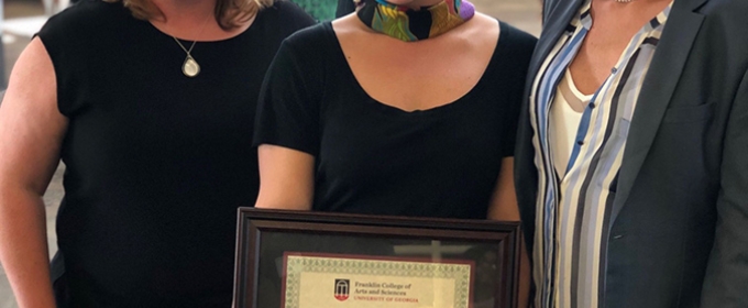 photo of three women, the middle holding a framed certificate