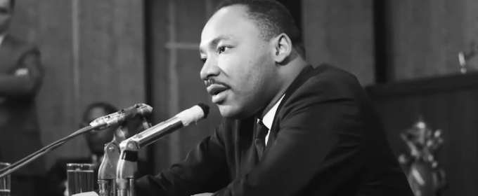 black and white photo of man seated at table with microphone