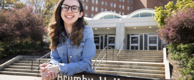 photo of woman leaning on dorm sign