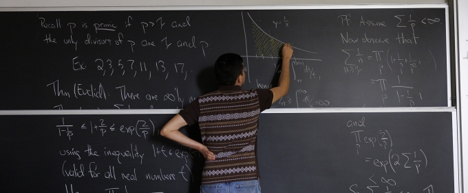 photo of person writing on chalkboard, back turned