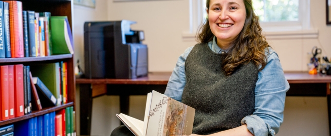 photo of woman sitting in chair with book, books shelves, and window 