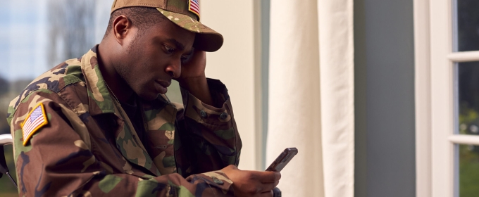 photo of man seated looking at cell phone