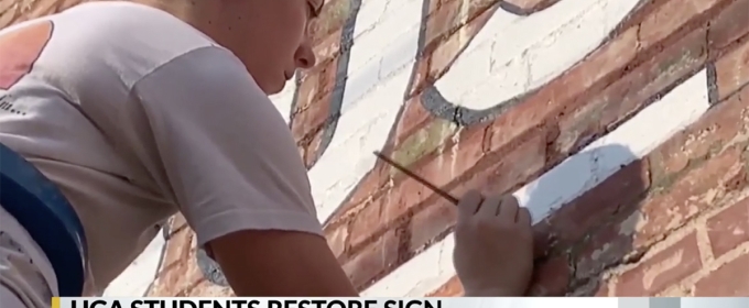 photo of woman painting letters on exterior brick wall