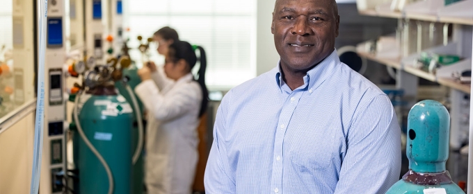 photo of man in lab, with people in lab coats, equipment in background