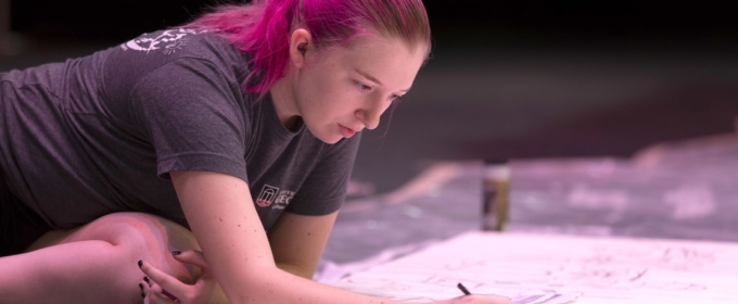 photo of woman leaning over a large drawing surface with pencils