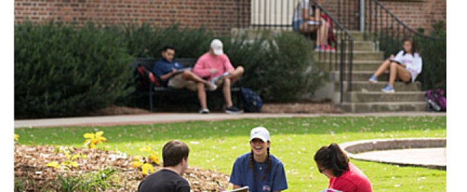 students sitting ton the ground in front of brick building